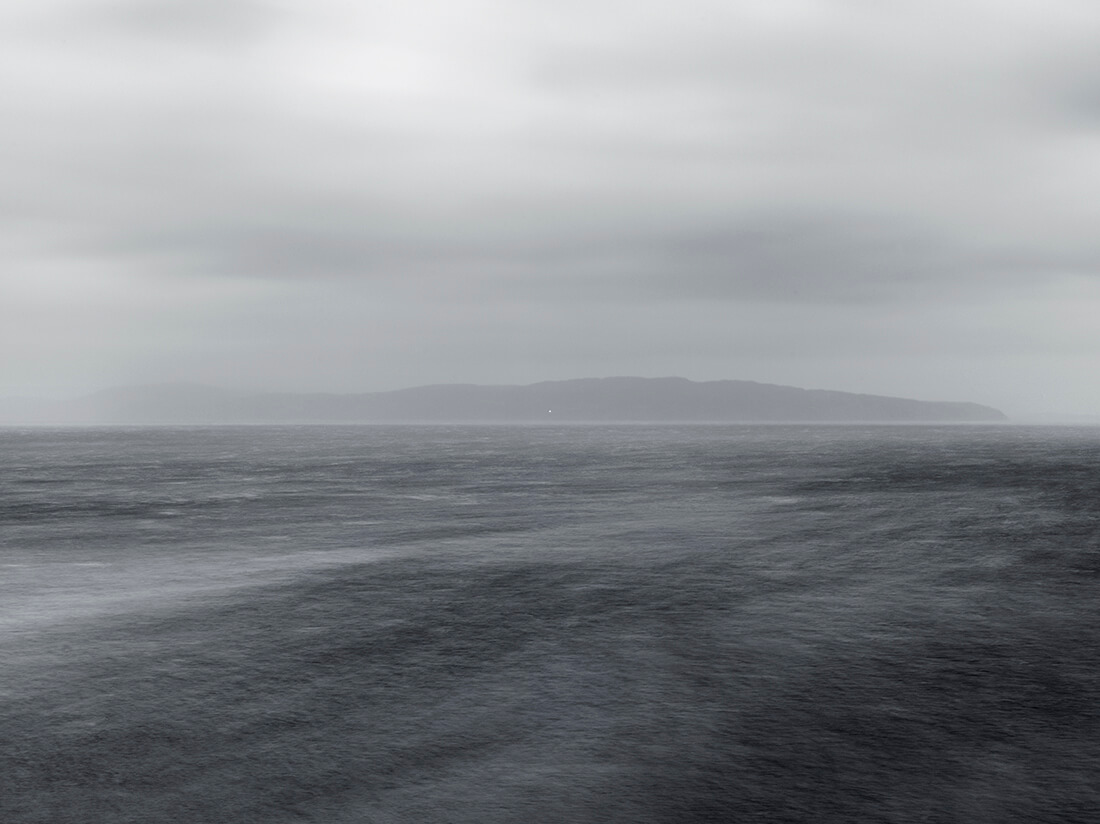 Photograph of a grey sea and overcast sky, coastline obscured by mist in the distance