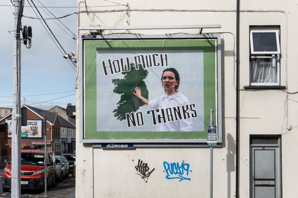 A billboard with an image of a person standing in front of a map of Ireland and the words 'How Much No Thanks'