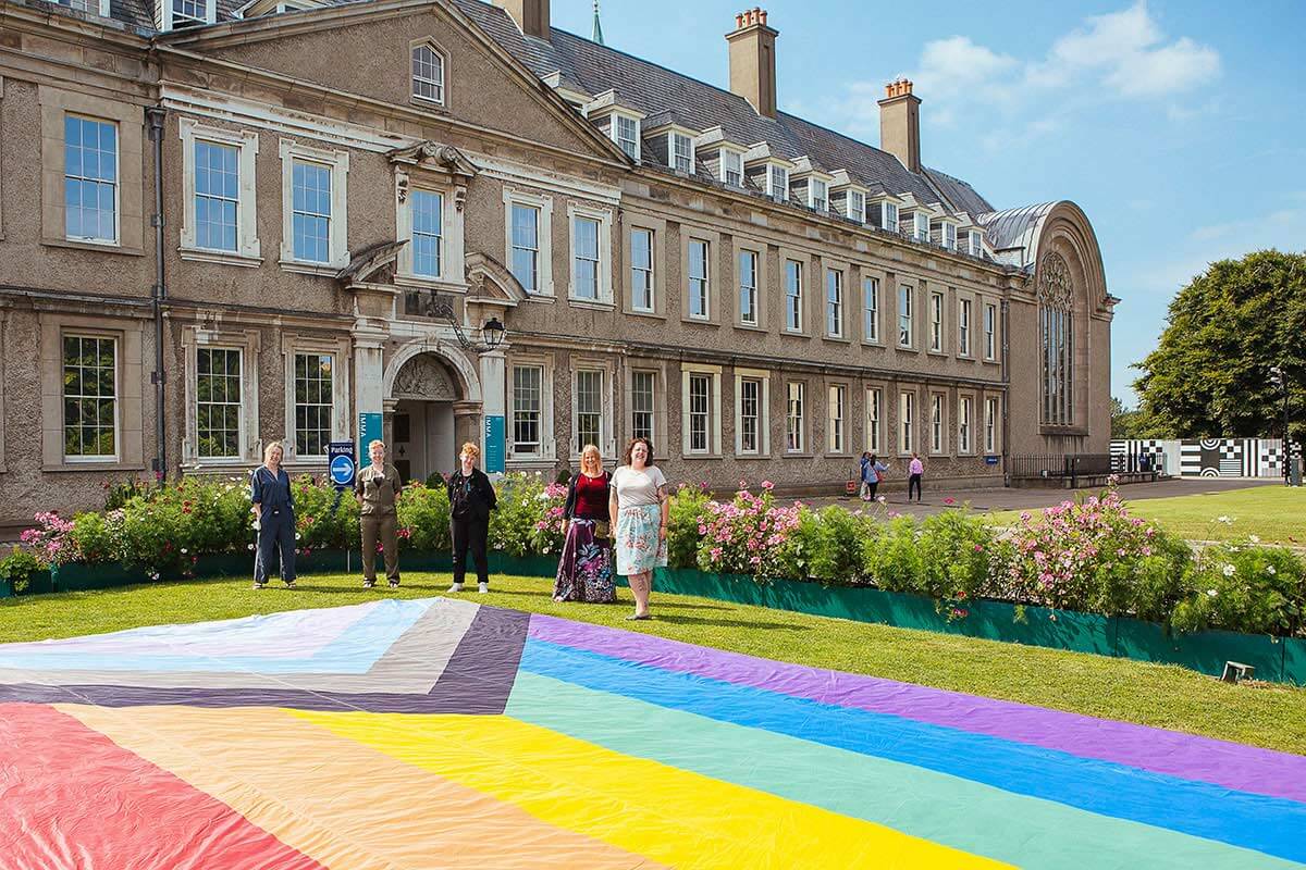 Exterior photograph of five people in front of IMMA. In front of them is a large pride flag spread out on the green.