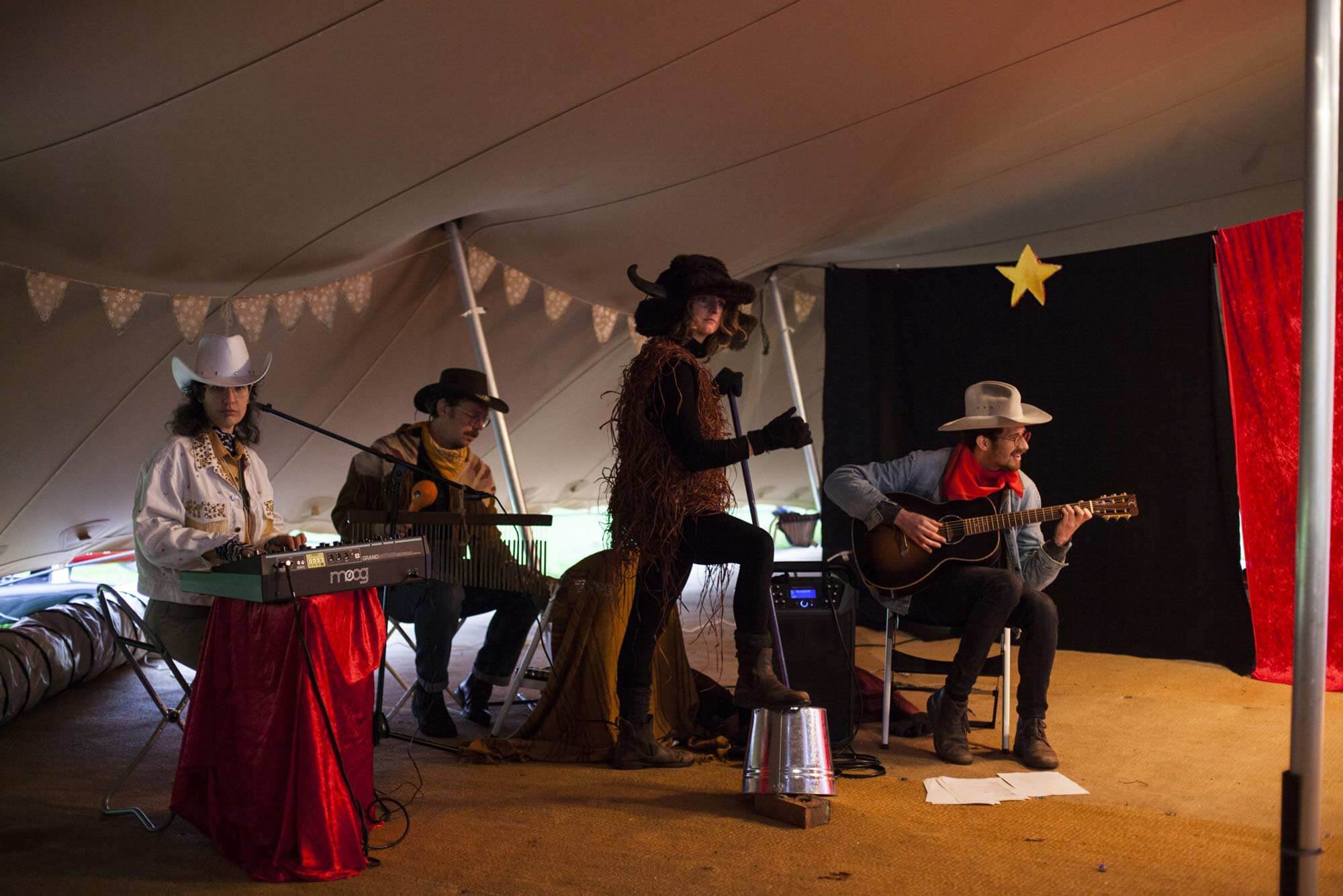 Interior photograph of four musicians in a tent, three dressed as cowboys and one as a buffalo