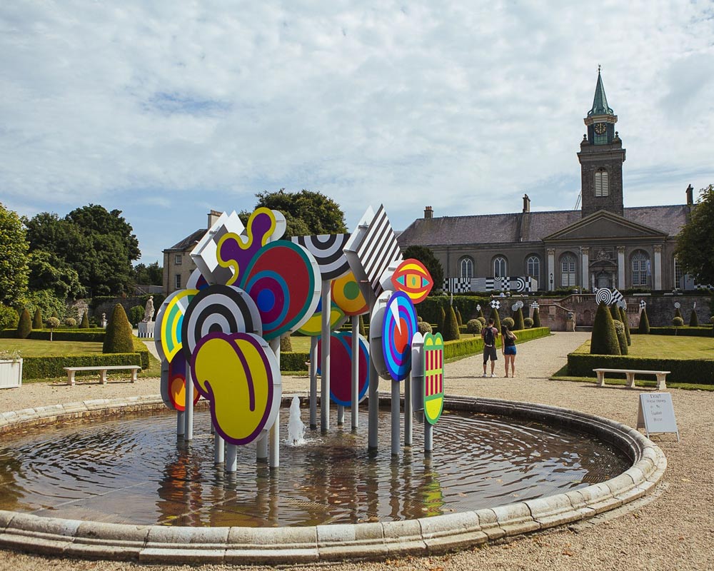 Exterior installation photograph of a fountain in a formal garden, an installation of colourful shapes in the centre of the fountain.