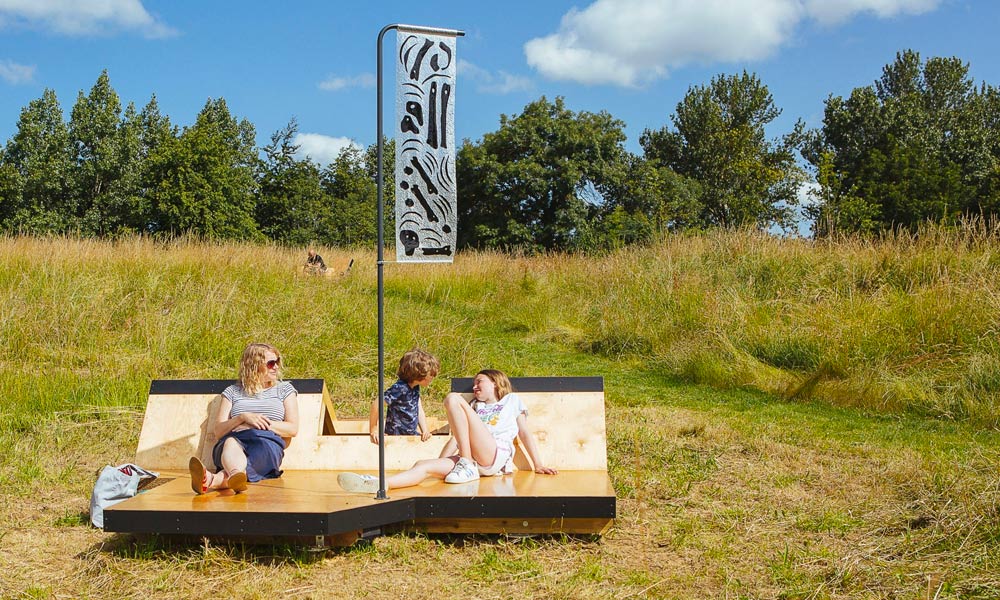 Photograph of a wooden seating structure installation in the meadow with a family sitting on it