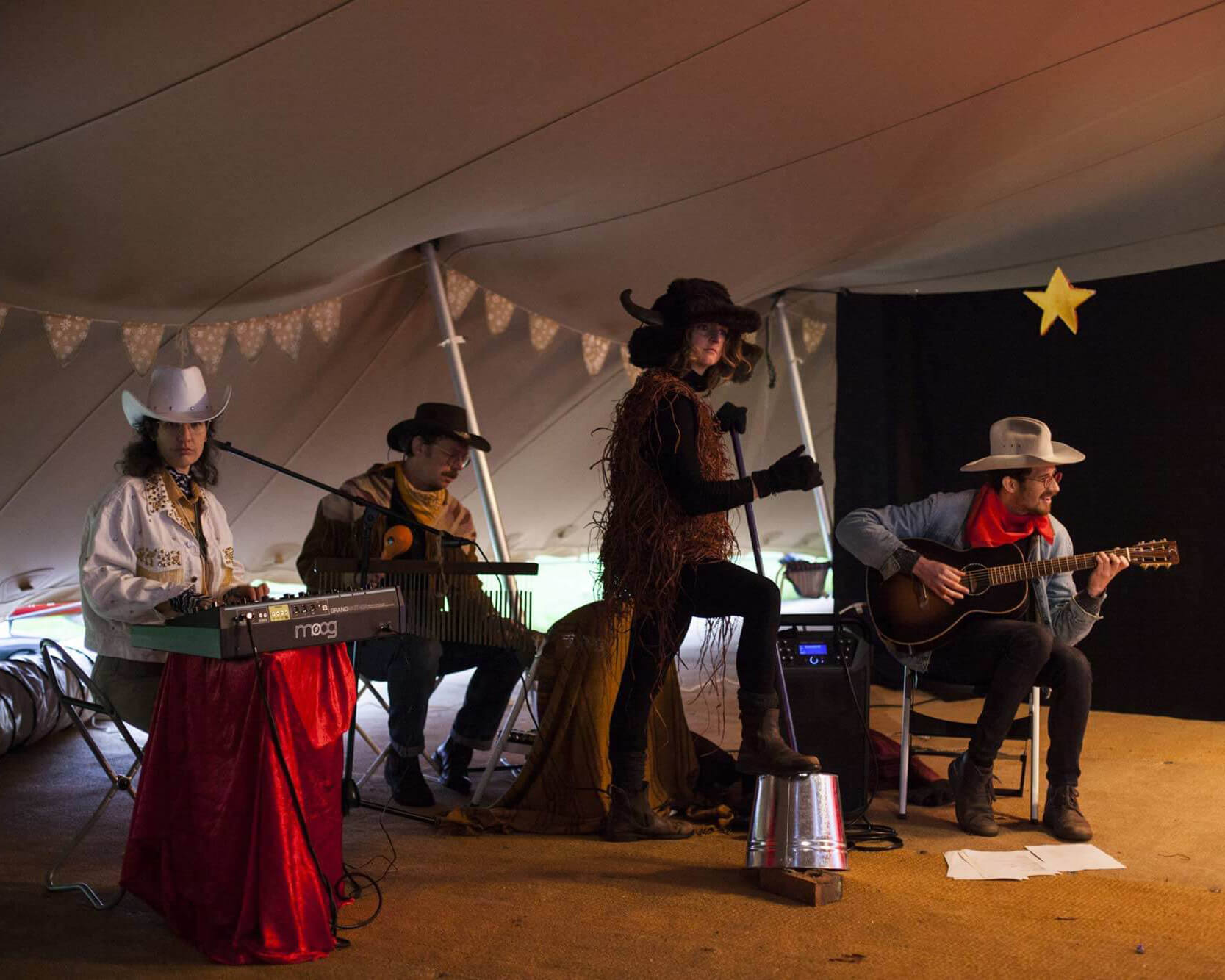 Interior photograph of four musicians, three dressed as cowboys and one as a buffalo.