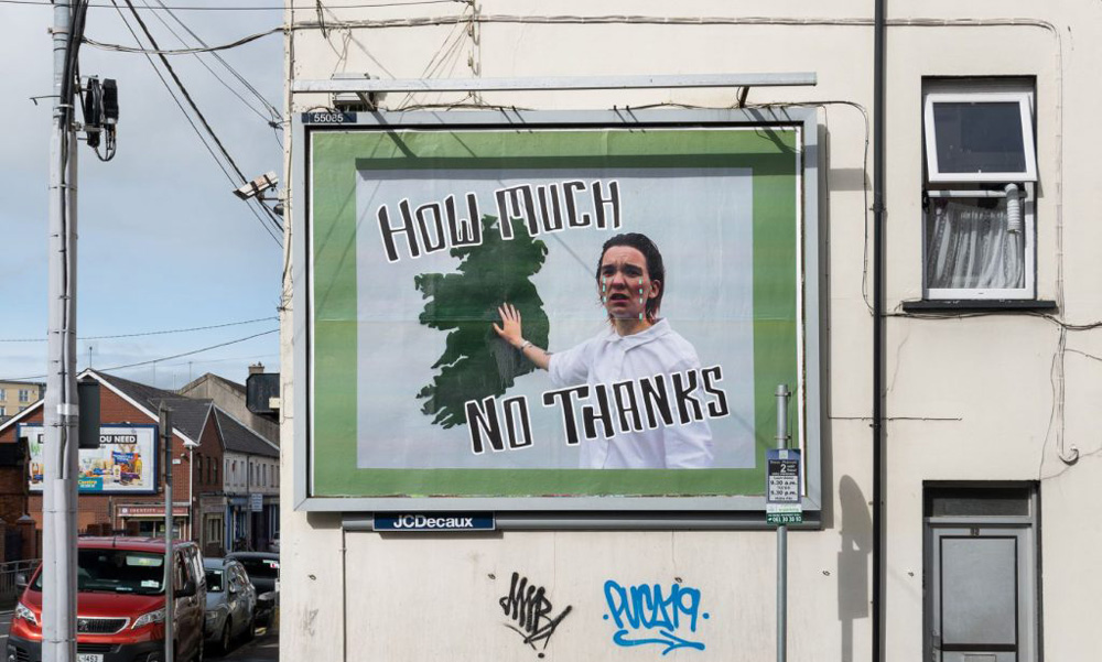 A billboard with an image of a person standing in front of a map of Ireland and the words 'How Much No Thanks'