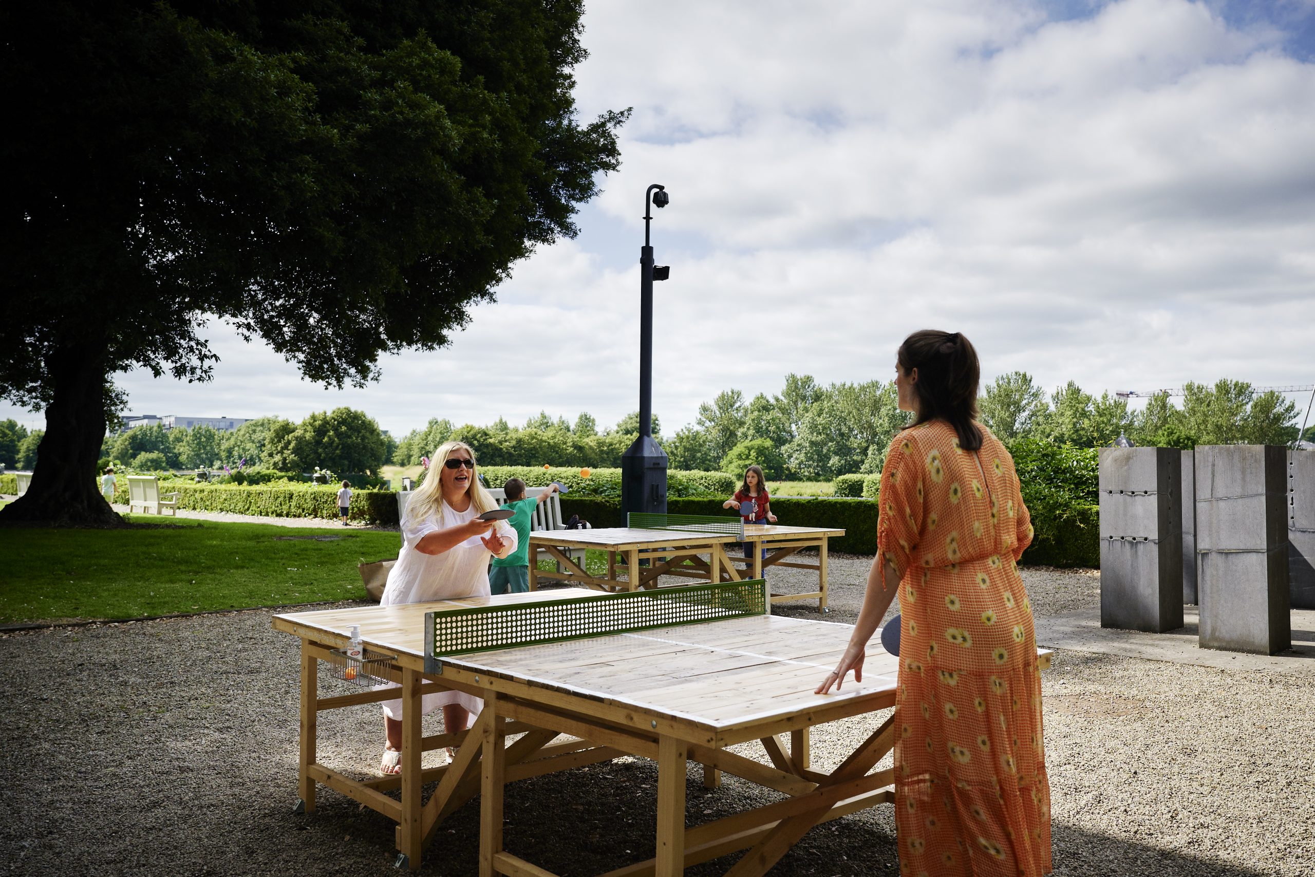 Photograph of two women playing on a wooden outdoor table tennis table.