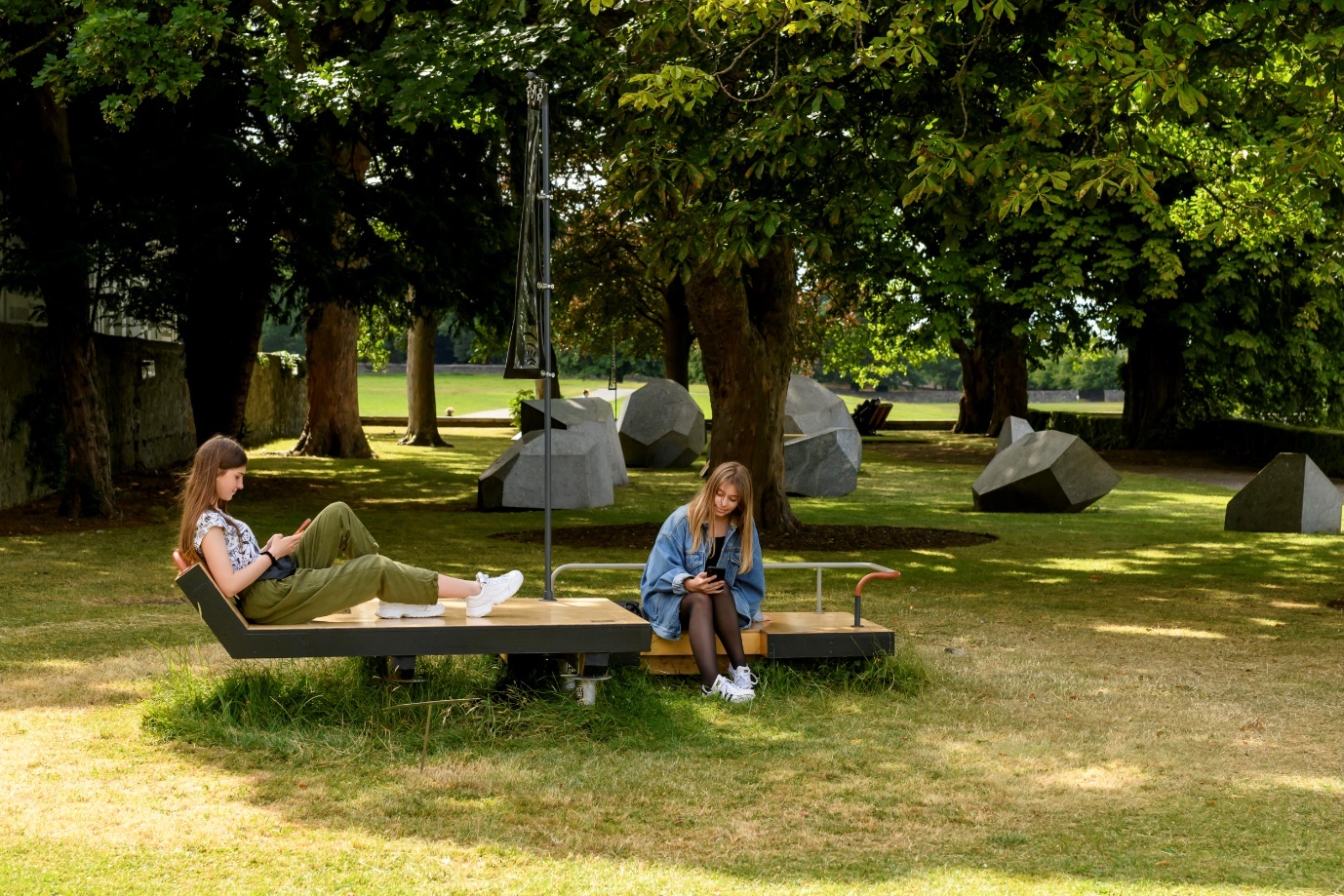 Exterior photograph of a wooden seating structure installation with two girls seated on it.